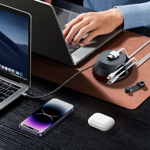 A desk setup with a laptop, smartphone, cable organizer, and wireless earbuds.