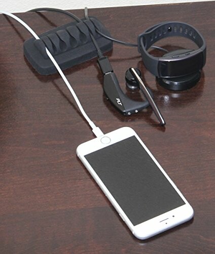 Smartphone with charging cable, smartwatch, and Bluetooth earpiece on a desk.